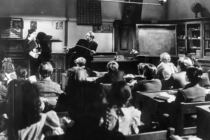 Lehrer mit Stock ermahnt Schüler in einer Klasse, die an eine Schule im Mittelalter erinnert.